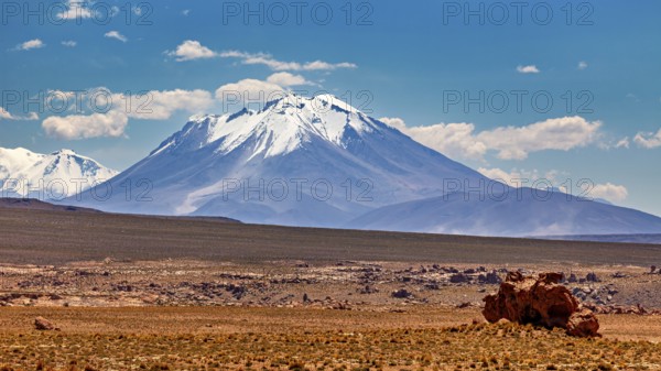 Snowy mountain in front of a vast desert panorama under clear, blue sky, the landscape of the Altiplano in Bolivia