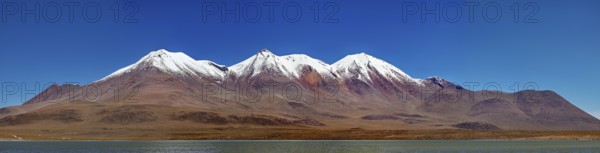 Snow-capped mountains above a desert plateau are reflected in a calm lake under a clear blue sky, Laguna Colorada in Altiplano in Bolivia