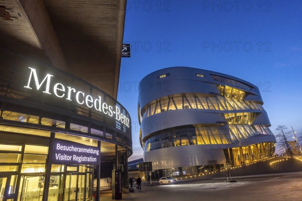 The Mercedes-Benz Museum in Stuttgart presents a journey through the automotive history of the global corporation. Spectacular architecture of the Automobile Museum in the evening. On the left, the entrance to the Mercedes-Benz Group AG factory premises. Stuttgart, Baden-Württemberg, Germany