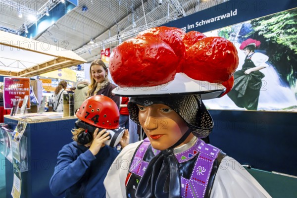 Tradition and progress. A young trade fair visitor wearing 3D glasses next to a model of a woman wearing traditional traditional costume and a Black Forest Bollenhut. Caravan — Motor — Tourism trade fair in Stuttgart. According to the exhibition organizer, CMT is the world's largest public trade fair for tourism and leisure. Stuttgart, Baden-Württemberg, Germany