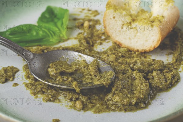 On a platter is a pesto sauce made from fresh basil, with a slice of bread and a spoon on a plate. The pesto sauce looks creamy and green, and the bread is partially eaten