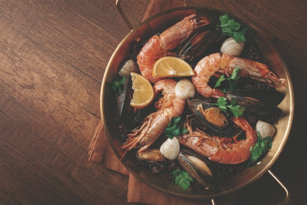 Seafood and black rice paella, in a frying pan, homemade, on a wooden table, no people