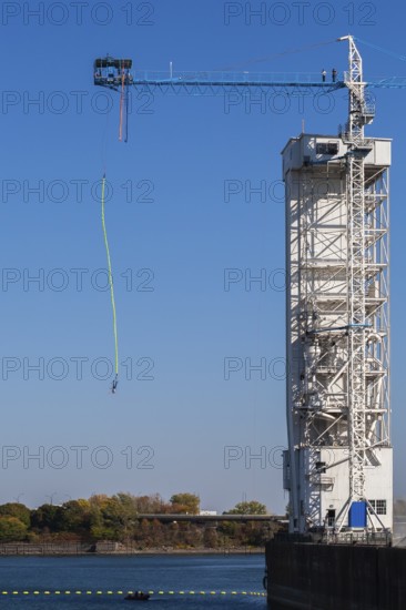 Montreal Bungee Tower with male bungee jumper in midair with his ankles tied to a long yellow elastic bungee jumping cord, Old Port of Montreal, Quebec, Canada