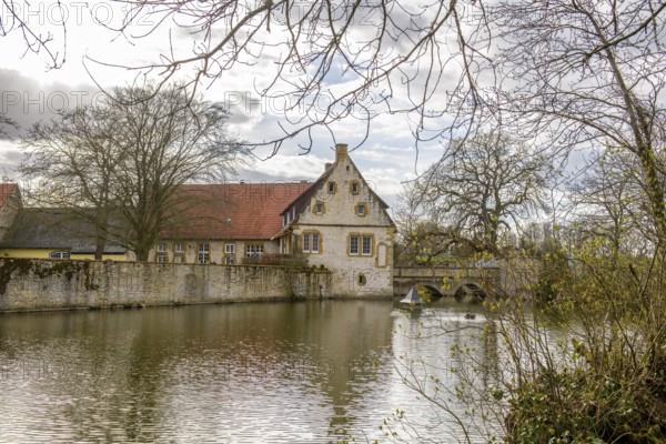 An old moated castle in Melle Haus Sondermühlen with bridge, surrounded by a large pond and trees Melle, Lower Saxony, Germany