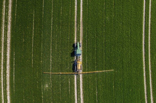 Aerial view over agricultural trailed field sprayer pulled by tractor spraying crop on farmland, field with pesticides, insecticides in spring