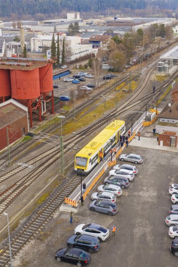 Aerial view of a train station with a yellow train surrounded by parking lots and industrial buildings, taking the Hermann Hesse Railway, Weil der Stadt, Black Forest, Germany