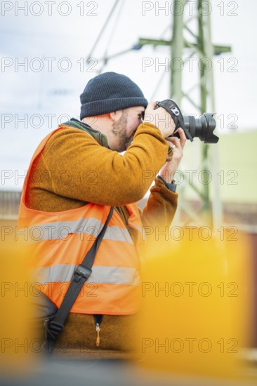 Person with camera wearing safety vest focused in industrial environment, Hermann Hesse Bahn journey, Calw, Black Forest, Germany