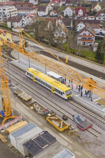Yellow train under crane on modern construction site, surrounded by urban residential area, acceptance of the Hermann Hesse Railway, Althengstett, Black Forest, Germany