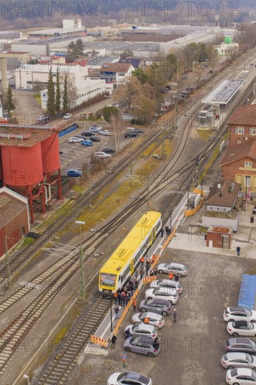 Yellow train at a train station surrounded by vehicles and buildings from a bird's eye view, taking the Hermann Hesse Railway, Calw, Black Forest, Germany