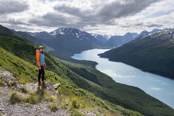 Female mountaineer enjoying views of blue lake and mountains on Twin Peaks Trail, Eklutna Lake, Chugach Mountains, Chugach State Park, Alaska, USA