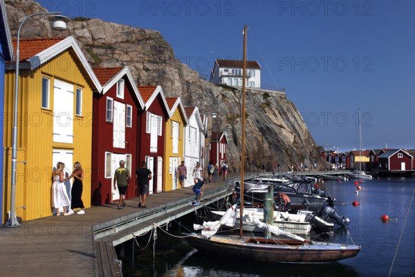 Lively harbor scene with colorful boathouses and walkers along the promenade, Smögen, Västra Götaland, Sweden