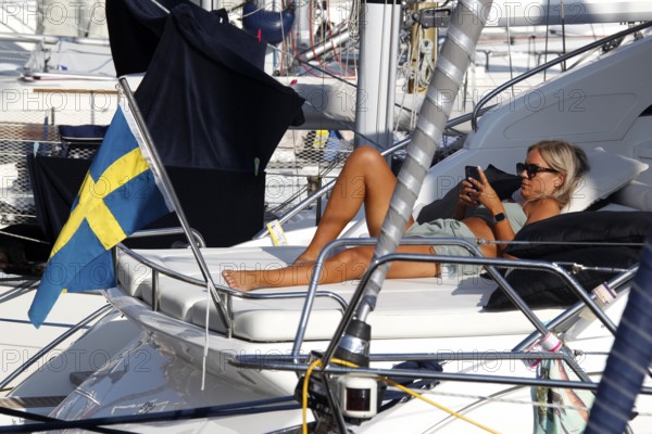 Woman relaxing on a sailboat with Swedish flag in harbor, Smögen, Västra Götaland, Sweden