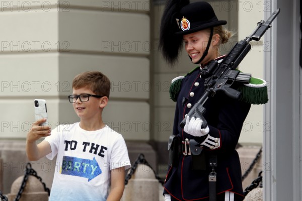 Child takes selfie with security guard in uniform in front of the Royal Palace in Oslo, Oslo, Norway