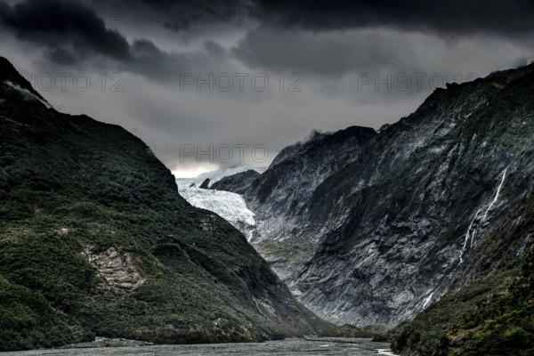 The Franz Josef Glacier with dramatic skies and steep, forested mountain slopes, Franz Josef, West Coast, New Zealand