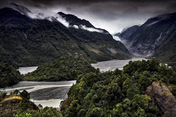 Franz Josef glacier stretches through a wooded valley under an ominous sky, Franz Josef, West Coast, New Zealand