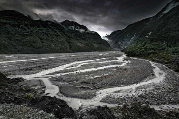Franz Josef glacier flanked by an extensive riverbed and under dark clouds, Franz Josef, West Coast, New Zealand