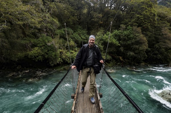 Person standing on a suspension bridge over a fast river, Fjordland National Park, New Zealand