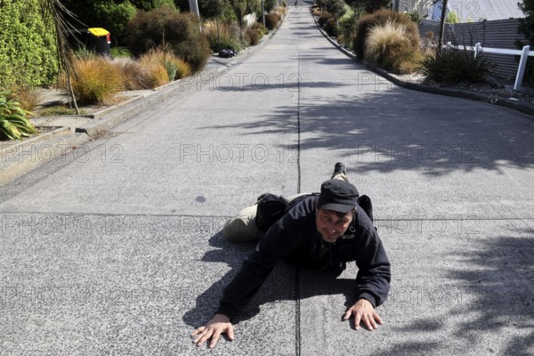 A person humorously lies on steep Baldwin Street in Dunedin, Dunedin, zero, New Zealand