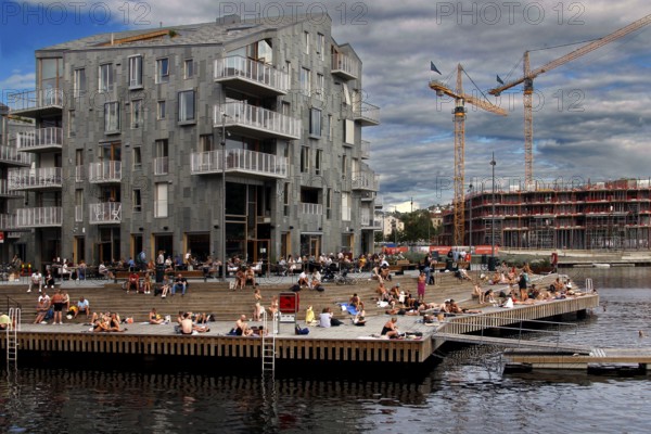 People enjoy summer on the shore next to modern buildings, Oslo, Norway