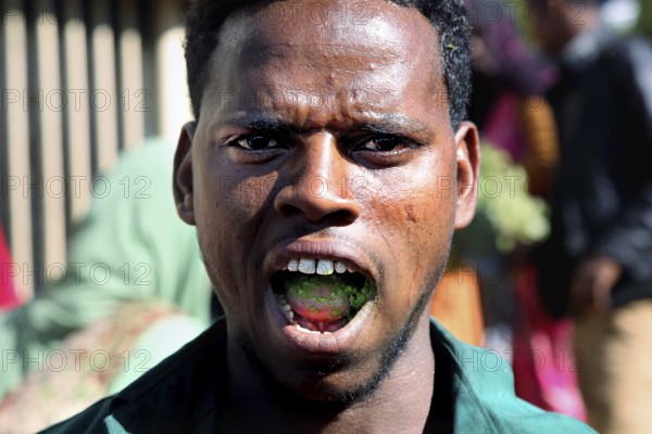 Man with khat leaves in his mouth smiles during lively market activity, Awaday, Afar, Ethiopia