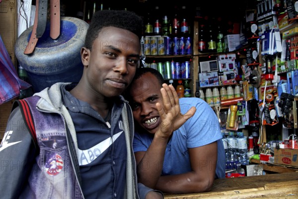 Two men stand in front of a well-equipped shop at a local market, Awaday, Afar, Ethiopia