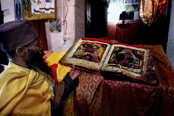 Priest in St. Mary's Cathedral in Axum holding an opened Bible with rich icon images, Axum, Tigray, Ethiopia