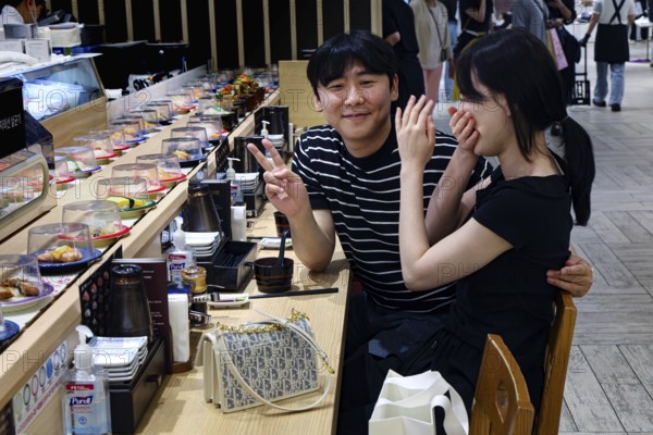 Friends enjoy sushi and laugh at lively restaurant, Busan, South Korea