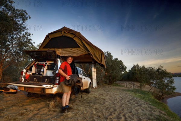 A riverside camp with roof tent and vehicle, surrounded by dusk, Pentecost River, Western Australia, Australia