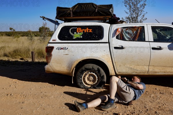 Person repairs flat tire next to a car in Purnululu National Park, Purnululu National Park, Western Australia, Australia