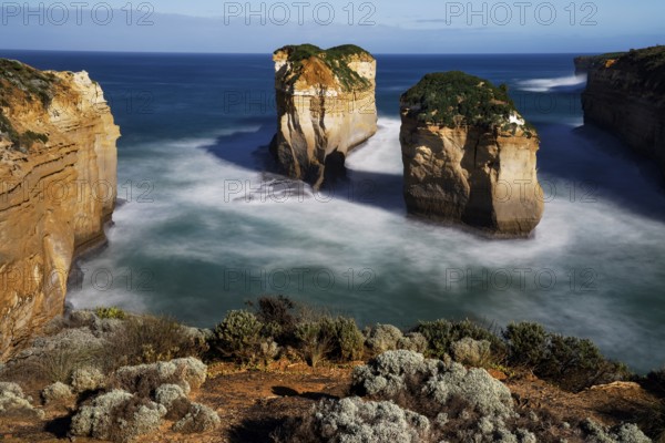 Impressive rocks rise from a calm sea under a blue sky, zero
