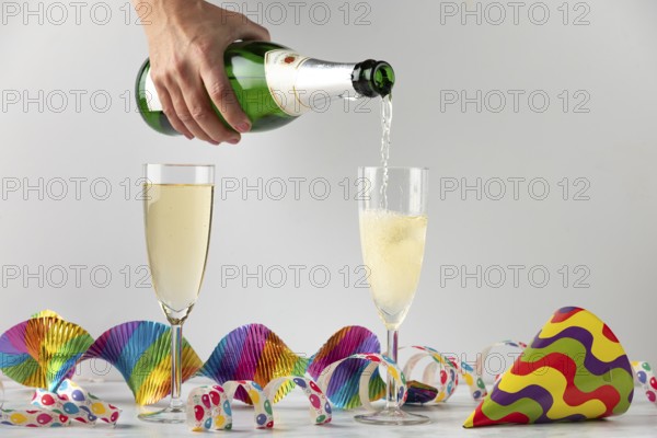 Sparkling wine is filled into glasses surrounded by colorful streamers, carnival