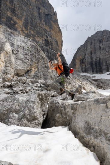 Mountaineer jumping off a rock into the snow, Camosci Valley, Brenta Mountains, Brenta-Adamello Natural Park, Trentino, Italy