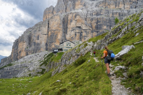Female mountaineer on a hiking trail in front of Rifugio Maria E Alberto Ai Brentai, mountainous landscape with steep rock faces, Brenta-Adamello Natural Park, Trentino, Italy