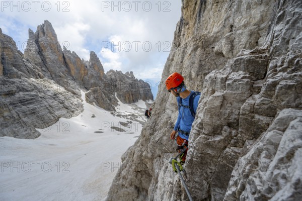 Mountaineer climbs on a steep rock face in the Via Ferrata dell'Ideale via ferrata, spectacular mountain landscape with steep rock faces, remnants of the Vedretta d'Ambiez glacier in the back, Brenta Mountains, Brenta-Adamello Nature Park, Trentino, Italy
