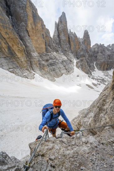 Mountaineer climbs on a steep rock face in the Via Ferrata dell'Ideale via ferrata, spectacular mountain landscape with steep rock faces, remnants of the Vedretta d'Ambiez glacier in the back, Brenta Mountains, Brenta-Adamello Nature Park, Trentino, Italy