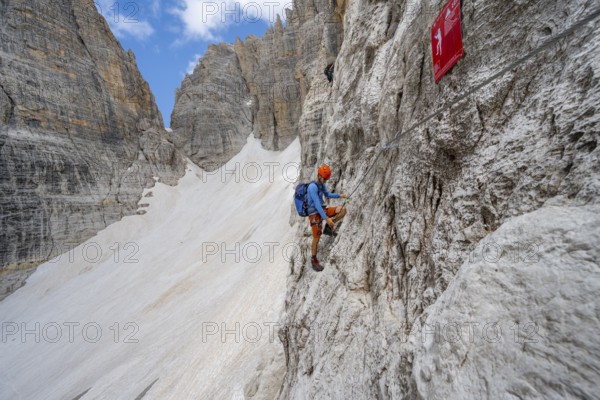 Mountaineer climbs on a steep rock face in the Via Ferrata Brentari via ferrata, spectacular mountain landscape with steep rock faces, remains of the Vedretta d'Ambiez glacier in the back, Brenta Mountains, Brenta-Adamello Nature Park, Trentino, Italy