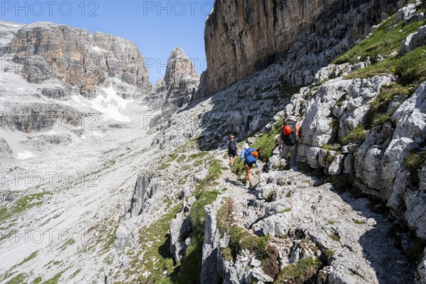 Three mountaineers on a hiking trail to Sella della Tosa, mountainous landscape in the Brenta Mountains, Brenta-Adamello Natural Park, Trentino, Italy