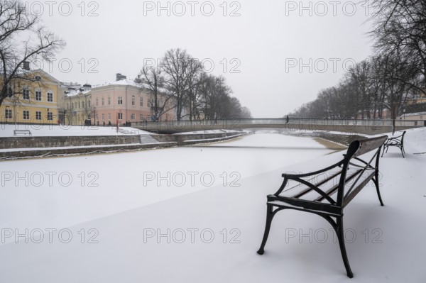 Bench, historic buildings on the frozen Aurajoki River, wintery Turku or Swedish Åbo, Varsinais-Suomi, Finland