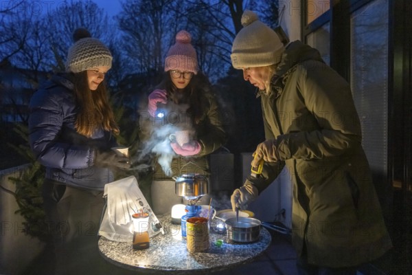 Symbolic picture blackout, extensive, prolonged power failure, in private surroundings, without electricity, heating, water, cooking, heating food and water with a gas-powered camping stove, on the balcony