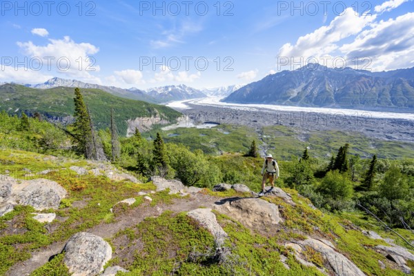 Young man on a hiking trail, view of impressive mountain landscape with Matanuska glacier and glaciated mountain peaks, Lion's Head, Chugach Mountains, Alaska, USA