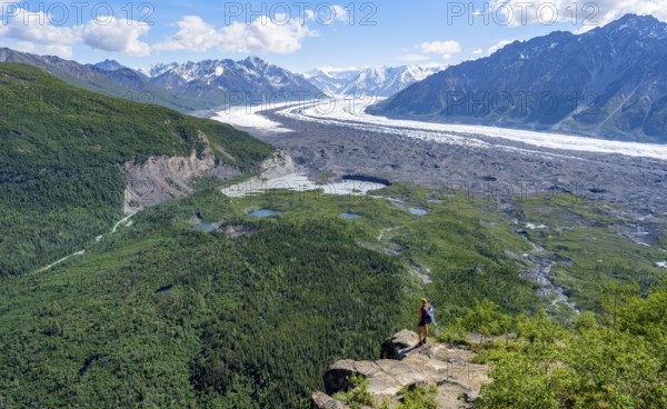 Young woman on a rocky outcrop enjoying the view, view of impressive mountain landscape with Matanuska glacier and glaciated mountain peaks, Lion's Head, Chugach Mountains, Alaska, USA