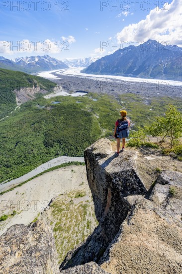 Young woman on a rocky outcrop enjoying the view, view of impressive mountain landscape with Matanuska glacier and glaciated mountain peaks, Lion's Head, Chugach Mountains, Alaska, USA
