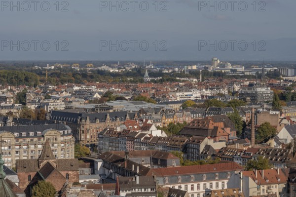 The stone balcony offers a view of the city of Strasbourg. Houses and buildings can be seen under a cloudy sky. Architectural details surround the balcony. Bas Rhin, Alsace, France