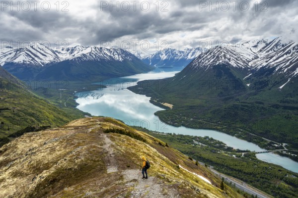 Climbers on a hiking trail on Slaughter Ridge, views of snowy mountains in spring and turquoise Lake Kenai Lake, Cooper Landing, Kenai Peninsula, Alaska, USA