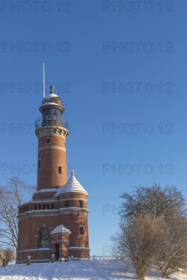 Holtenau lighthouse at the entrance of the Kiel Canal in winter, west bank of the Kiel Fjord, shipping, brick building from 1895, round tower, orientation, sea sign, beacon, ground floor with wedding room, trees, snow, blue sky, Baltic Sea, Kiel, Germany