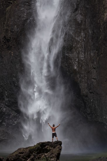 Daytime scene at Wallaman Falls with a fit man in swim trunks below the waterfall, Queensland, Australia