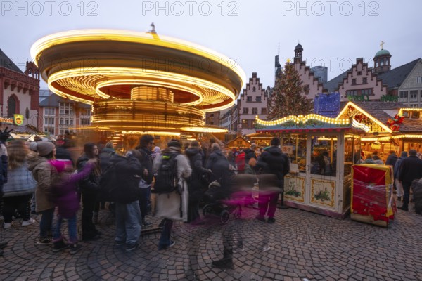 December 22, 2025, Frankfurt Christmas Market on Roemerberg with the skyline in the background at twilight. Lights are shining and a children's carousel is spinning, Frankfurt, Hesse, Germany
