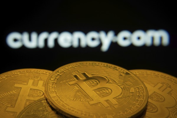 Dhaka, Bangladesh- 22 June 2025: Close-up of Bitcoin coins with the Currency.com logo visible on a screen in the background
