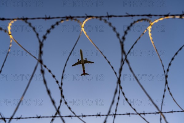 Symbolic picture security at the airport, outer fence at Düsseldorf International Airport, steel wire fence, with S-wire rollers, NATO wire, on the fence crown, airplane taking off, North Rhine-Westphalia, Germany
