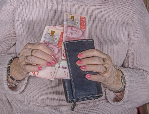 An elderly woman's hands take out Swedish banknotes from a wallet